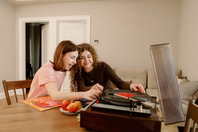 image shows two young teenagers putting a record on a record player together, smiling